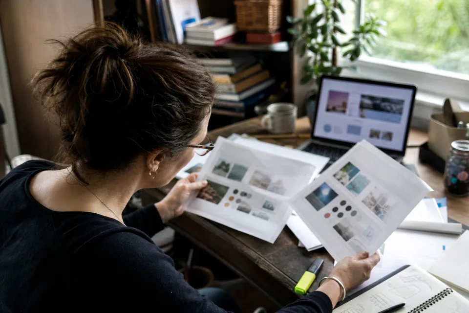 Business owner comparing two printed design proposals with a highlighter next to a laptop